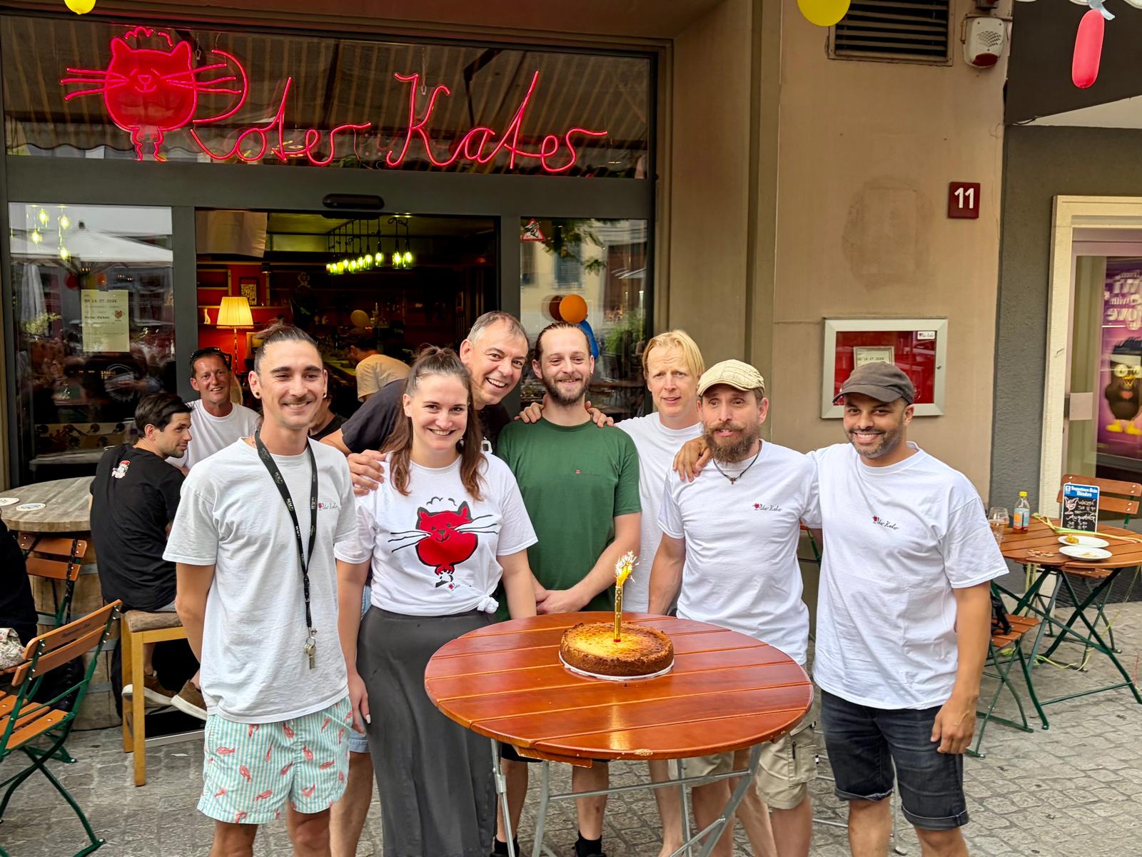 Das Team vom Roten Kater feiert den 1. Geburtstag vor dem Neon-Schild am Neumarkt 11
