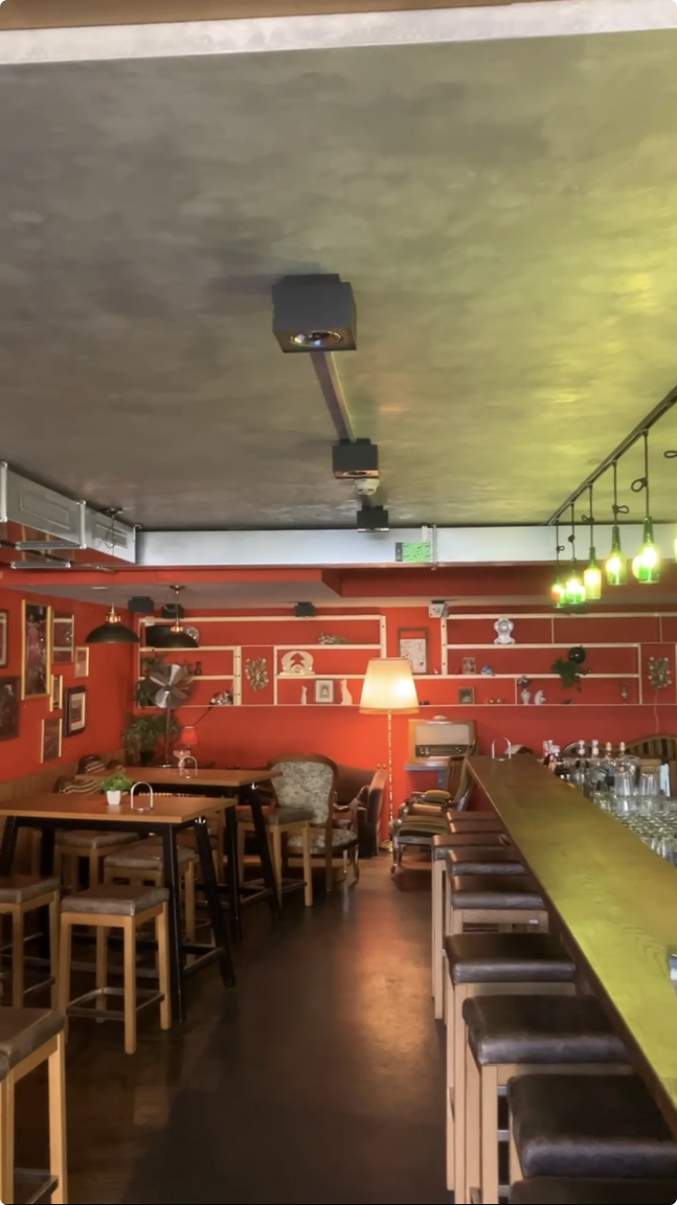 Innenansicht der Bar mit langem Tresen, roten Wänden und Regalen